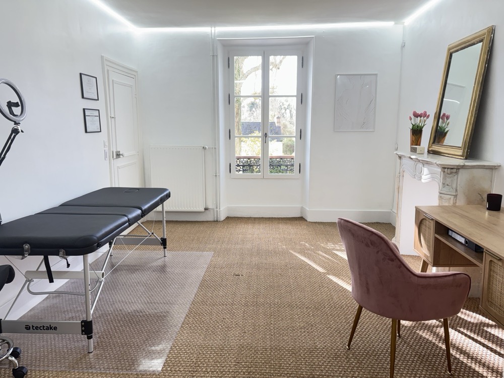 La pièce de l'institut : une fenêtre donnant sur le jardin, une table de soin, un miroir ancien, une cheminée en marbre et des tulipes roses.